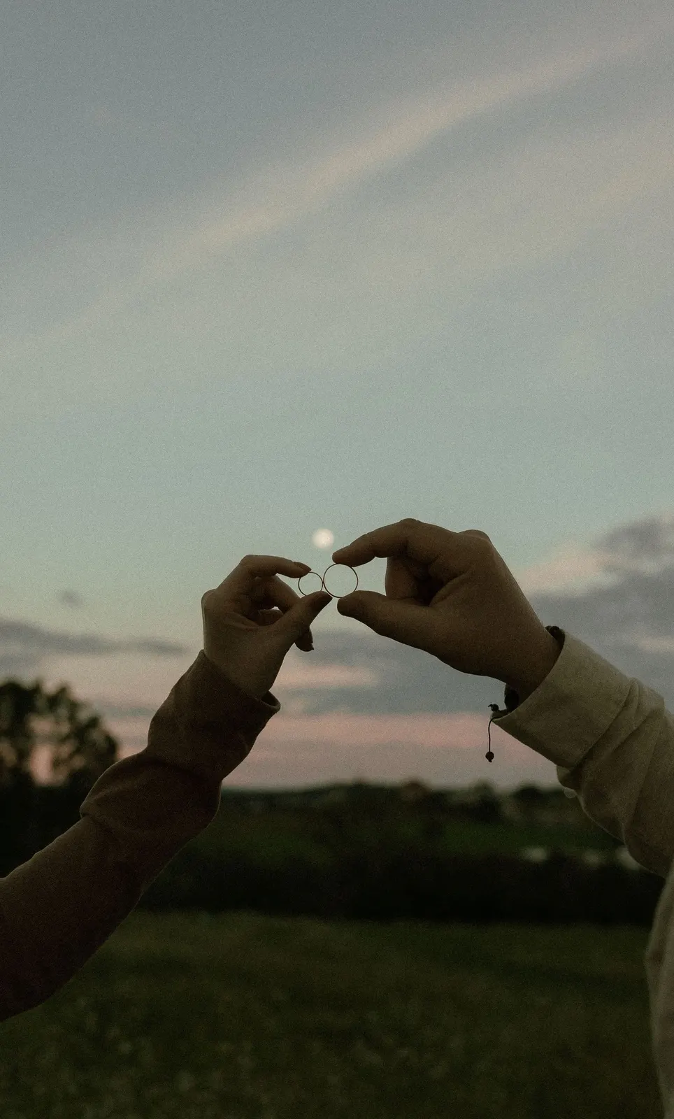 Two hands holding wedding rings against a sunset (sample image)