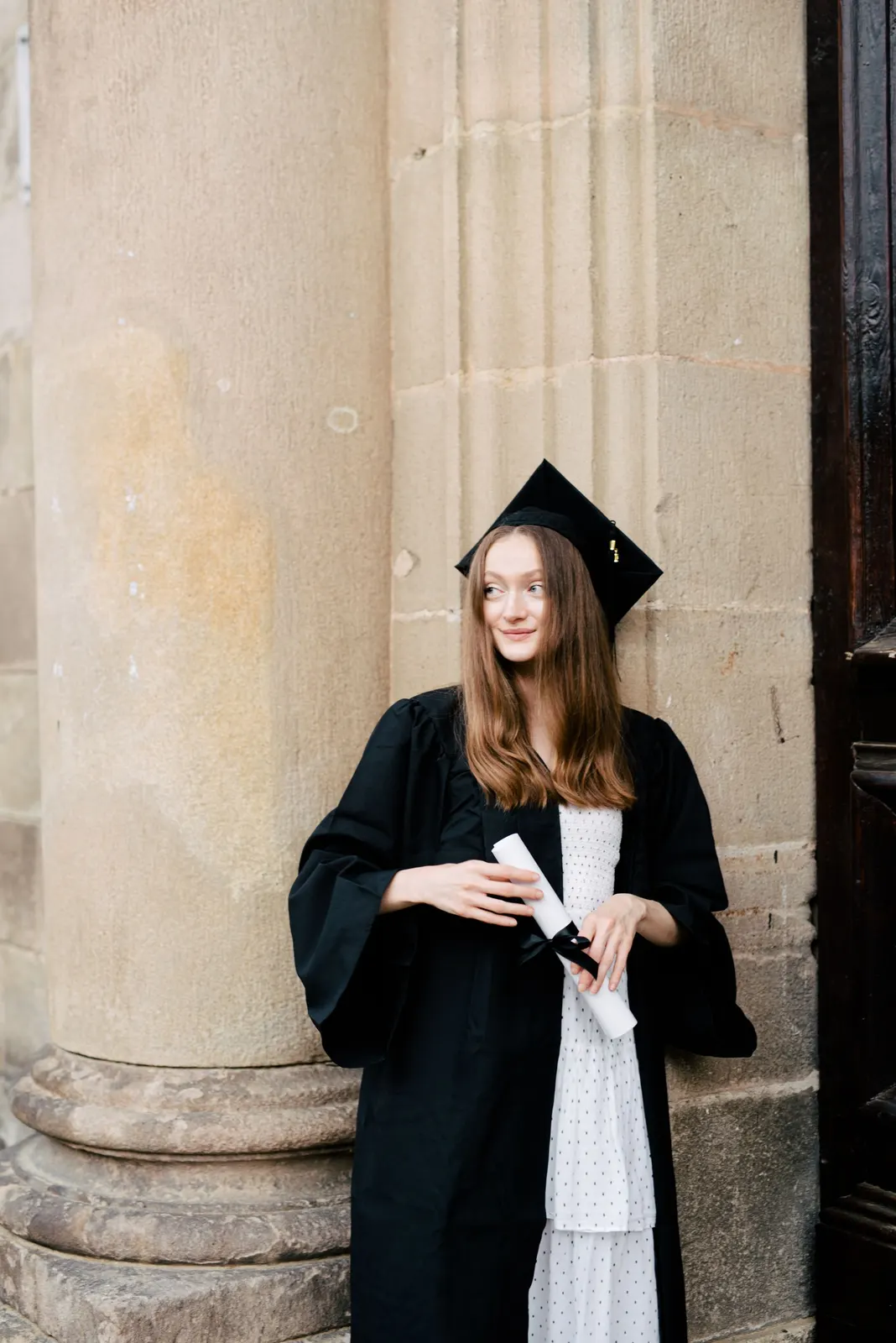 Graduate in cap and gown beside stone columns (sample image)