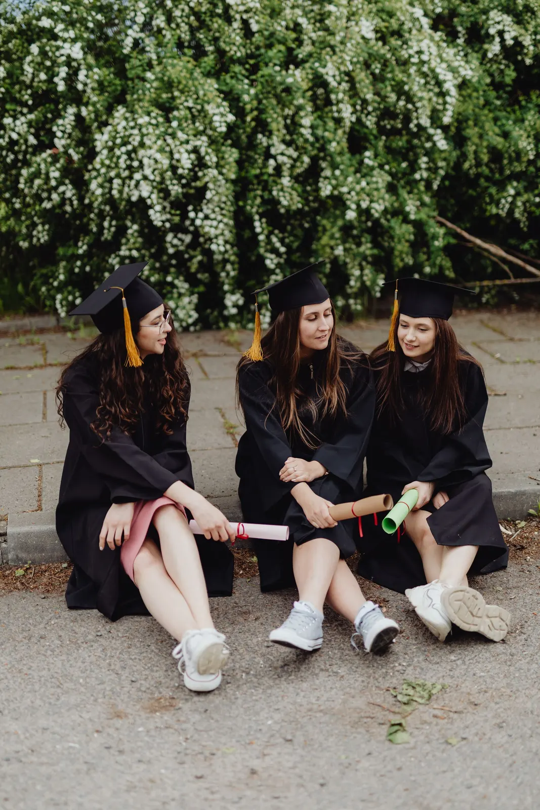 Three graduates in caps and gowns sitting outdoors (sample image)