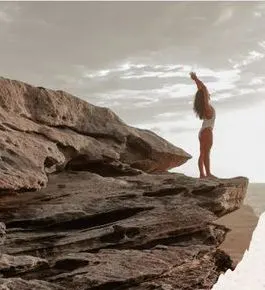 A woman with arms raised on a sandstone ledge at sunset, by 2819 Photography