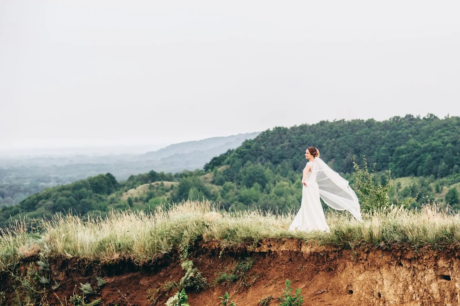Bride on a grassy hilltop with a long veil (sample image)